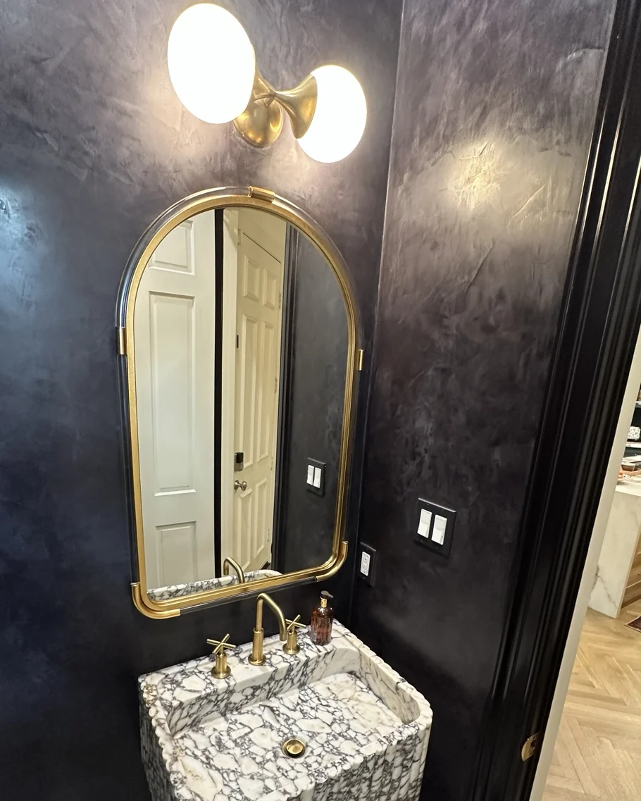 Arched gold mirror above a sculptural marble bathroom sink