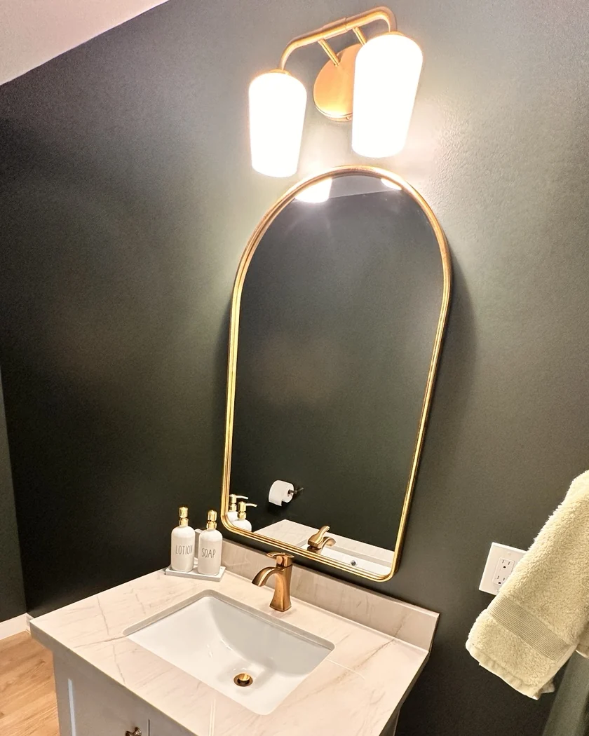 Gold-framed bathroom mirror with wall light above vanity